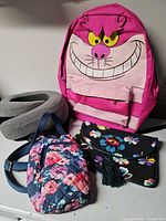 Group view of neck pillow, Cheshire Cat backpack, quilted water bottle holder, floral purse