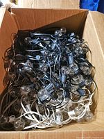 Cardboard box containing two intertwined café string lights, visible black and white cords with clear glass bulbs