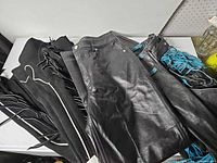 Overview of three garments: leather pants centered, suede chaps on left, leather chaps with blue fringe on right