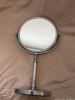 Front view of chrome tabletop vanity mirror showing round reflective surface and pedestal stand