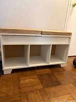 Front view of white bench showing three lower cubbies and two beige seat cushions