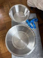 Two stainless steel pedicure bowls of different sizes with blue plastic link chain on mat