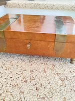 Closed jewelry box front view showing burl veneer, brass straps, keyhole, brass feet