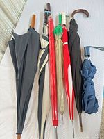 Seven collapsed umbrellas laid side by side showing canopy colors and handle types