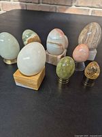 Group of eight stone eggs on metal and stone stands showing sizes and colours