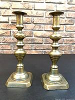 Front view of both brass candlesticks showing patina and square bases