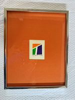 Framed abstract print centered in orange mat within silver frame