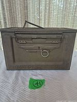 Front view of steel ammo box showing embossed "AMM.BOX CAL .50" marking, latch with pull ring and carry handle