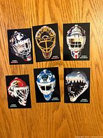 Six goalie mask cards displayed face up on wooden surface