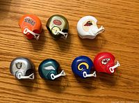 Seven miniature NFL plastic helmets displayed on wood surface