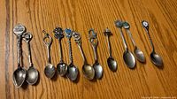Full set of eleven Canadian souvenir collector spoons laid on wooden surface