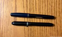 Two capped fountain pens on wood surface, blue Waterman above black Wearever