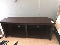 Front view of dark brown TV stand showing two open cubbies and cable holes