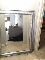 Front view of large silver framed mirror leaning against wall