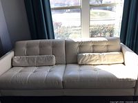 Front view of white leather tufted sofa with two lumbar pillows
