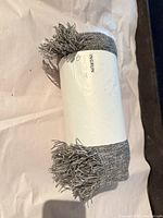 Rolled gray throw showing fringe and wrapper front
