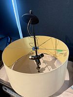 Top view of pendant showing black canopy, stem, wiring, spokes supporting large ivory fabric drum shade