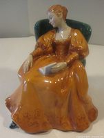 Front view of Royal Doulton Romance figurine showing seated woman in orange gown holding book