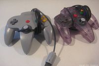 Top view showing grey and translucent purple Nintendo 64 controllers with buttons and cords
