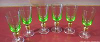 Front view of six green stemmed shot glasses showing color and gold ribbed stems