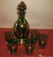 Front view of emerald green decanter with stopper and five matching glasses showing gold leaf design