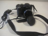 Front view of camera with lens cap, neck strap and cable