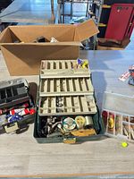 Overall lot showing green tackle box with trays extended, grey tackle box, clear lure case and cardboard box
