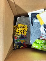 Top view of box showing grey shorts, black garment, yellow star-print pants