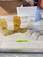 Two amber Pioneer Hotel boot mugs and two clear Dixie Stampede mini boot cups on table