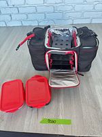 Overall view of black and red insulated meal-prep bag with front flap open showing interior shelves and two red containers beside