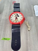 Full view showing oversized wristwatch design, red case, black strap, power cord