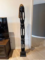 Full view of carved wood totem standing against wall