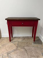 Front angled view of red console table showing drawer and legs