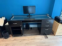 Front view of black glass-top desk with monitor on top