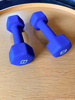 Two blue-purple 8 lb neoprene dumbbells on wooden surface