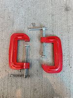 Two red metal C-clamps on concrete surface
