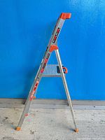 Full side view of folded Little Giant Flip-N-Lite aluminum step ladder showing three steps and orange accents