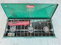 Full view of open stove showing three burners, red fuel tank and grate