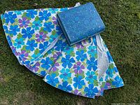 Three folded round floral tablecloths with matching blue floral suitcase displayed on grass