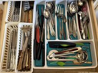 Drawer open showing full assortment of cutlery, knives, and utensils in white and teal organizers