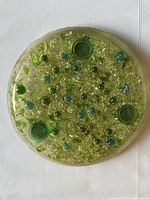 Top view of full round lucite trivet showing embedded green and blue elements