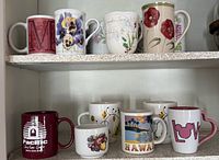 Front view of two shelves holding eleven assorted ceramic mugs in various designs