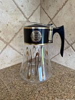 Left side view of carafe showing handle, collar medallion and gold teardrop design