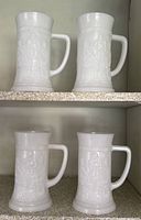 Four matching white milk glass steins on shelves