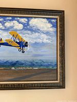 Close view of framed painting showing Stearman PT-17 aircraft, runway, mountains and detailed frame edge