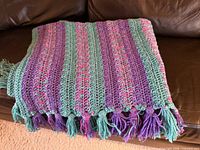 Folded striped crochet afghan in lavender, mint and pink with tassels