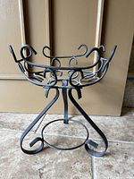 Front view of wrought iron plant stand showing tripod legs, lower stretcher ring and upper scroll ring