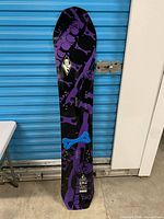 Full snowboard front view leaning against wall showing graphics and length