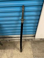Sword sheathed in black scabbard, full length view