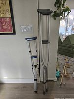 Pair of adult adjustable crutches and folded travel crutch standing against wall